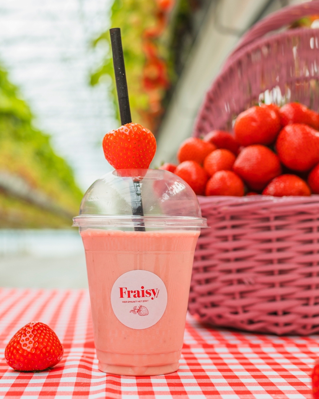 Een roze aardbeienmilkshake met een verse aardbei op het rietje, op een geruit tafelkleed.