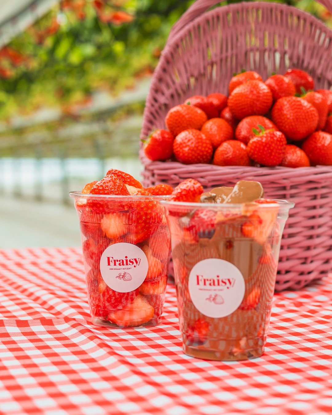 Bekers met verse aardbeien en met aardbeien in chocolade, op een rood-wit geruit tafelkleed.