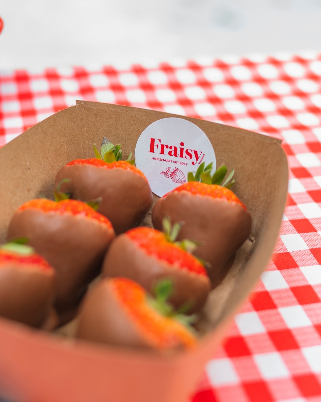 Verse aardbeien en aardbeien in chocolade in Fraisy-bekers, op een rood-wit geruit tafelkleed.